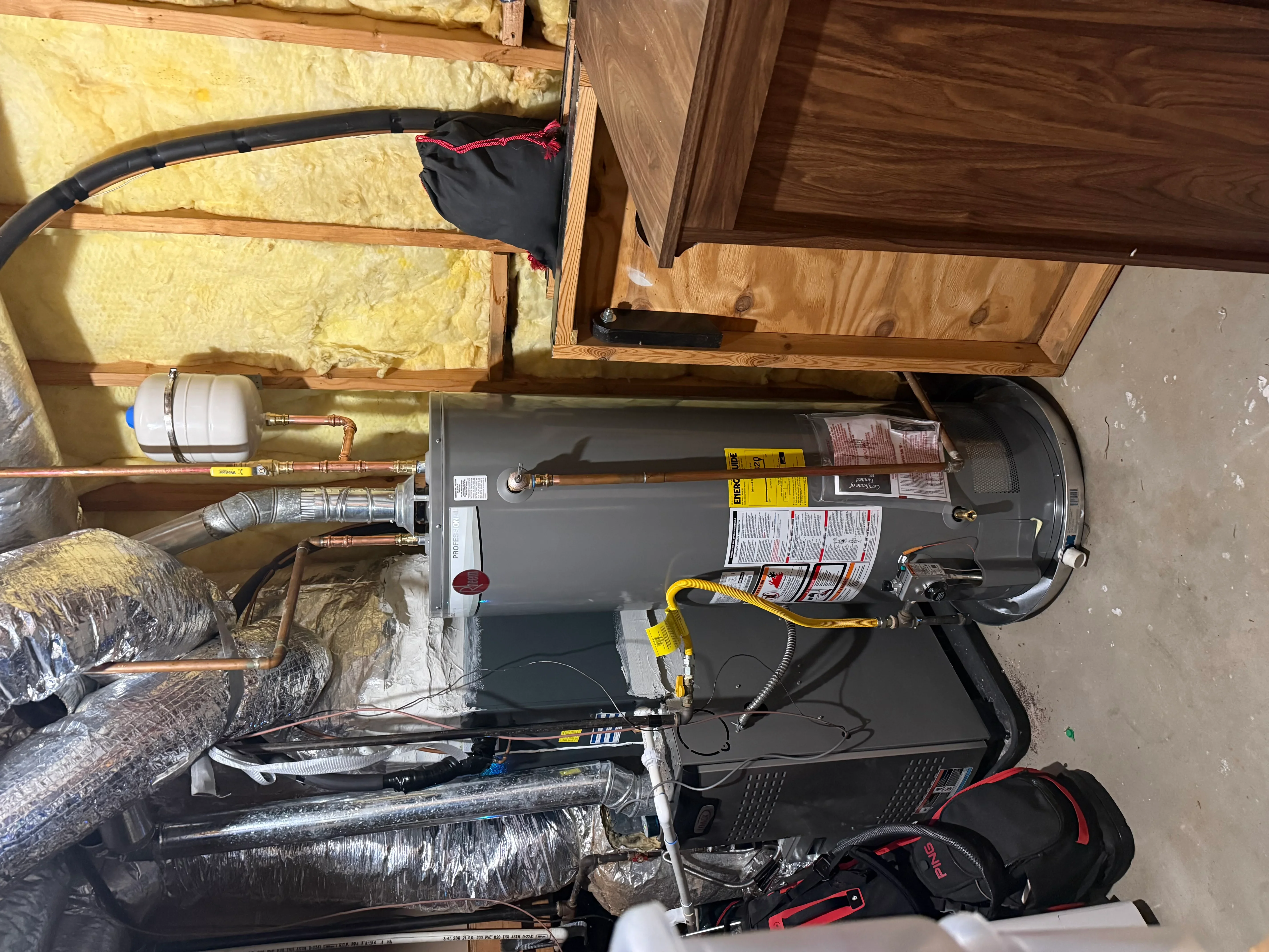 New electric water heater installation with copper piping and safety connections in framed utility space