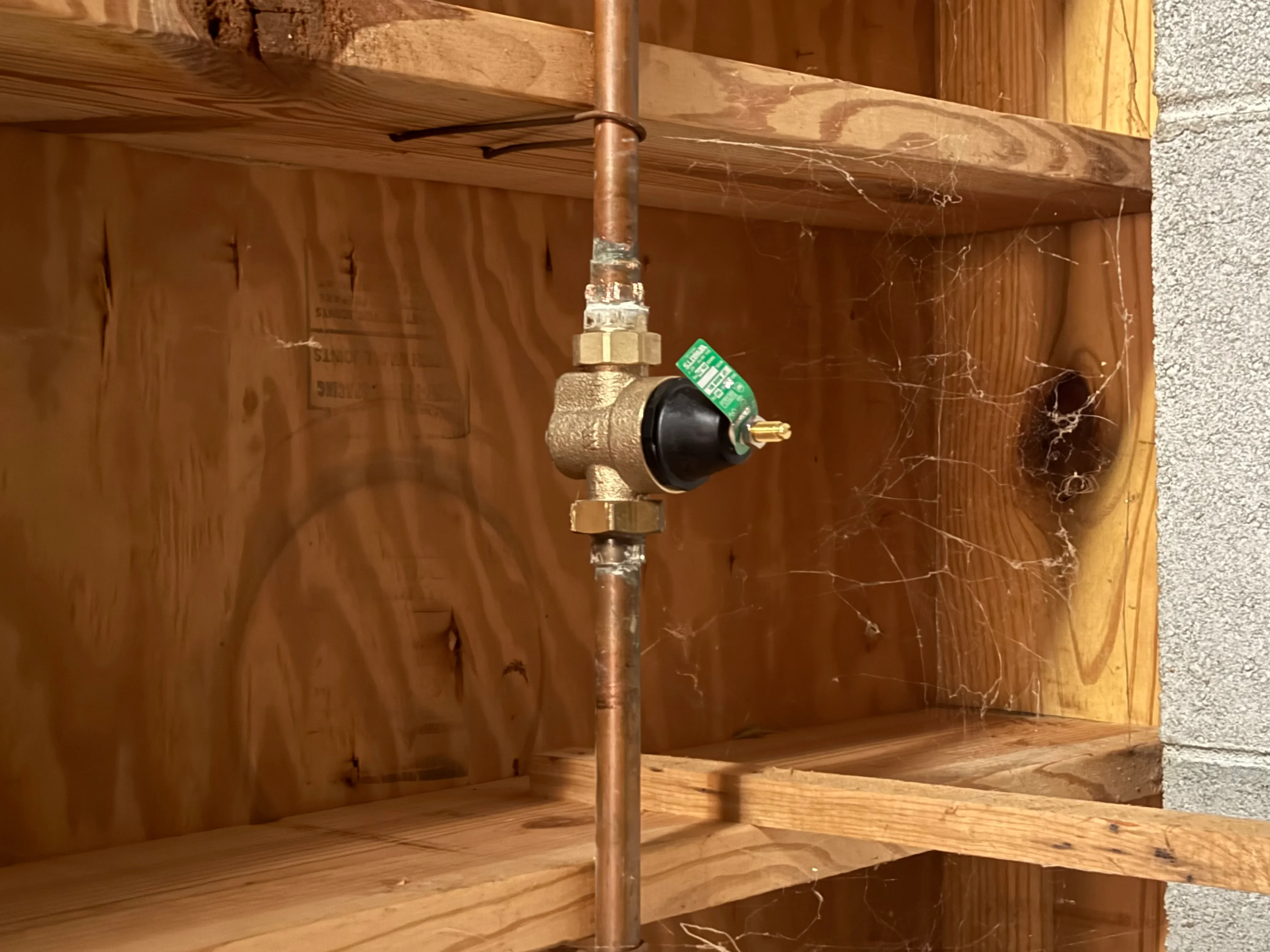 Copper water line with brass pressure regulator valve installed in wooden framed structure