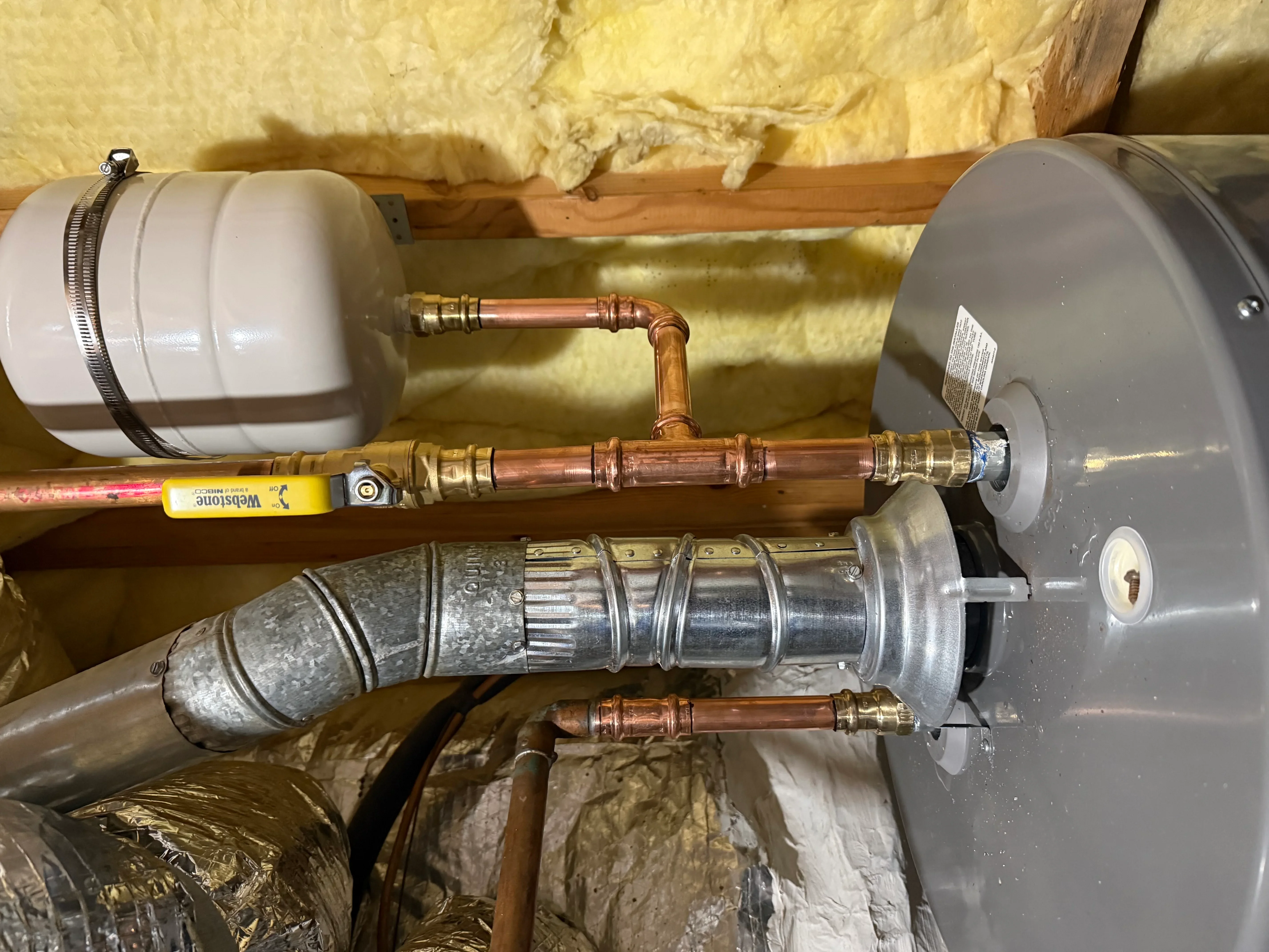 Installed water heater system with expansion tanks, copper pipes, and brass fittings in attic